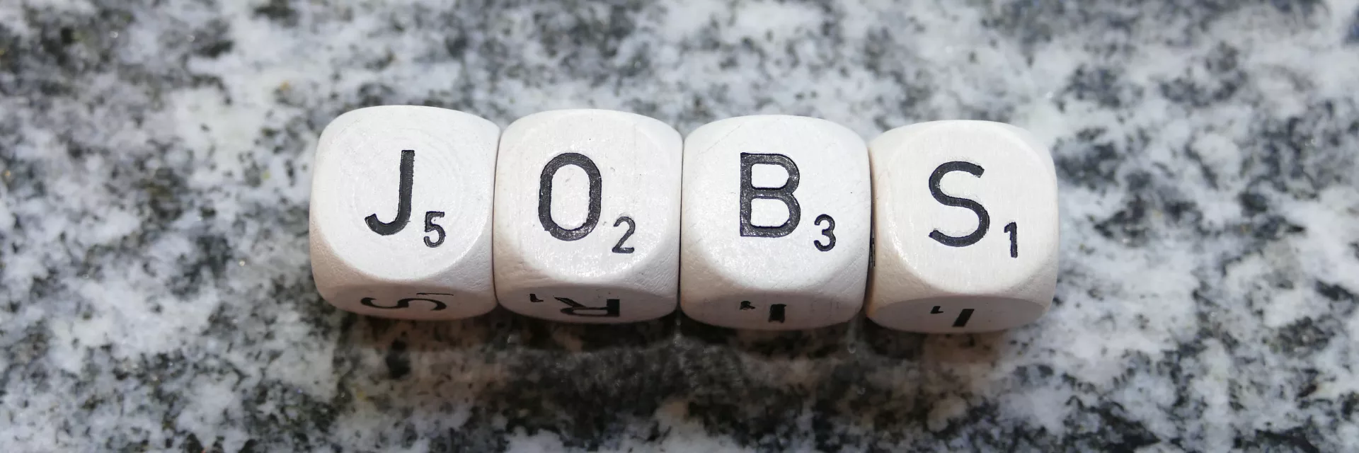 auf einer Granitplatte liegen 4 Buchstaben-Würfel und bilden das Wort "JOBS"