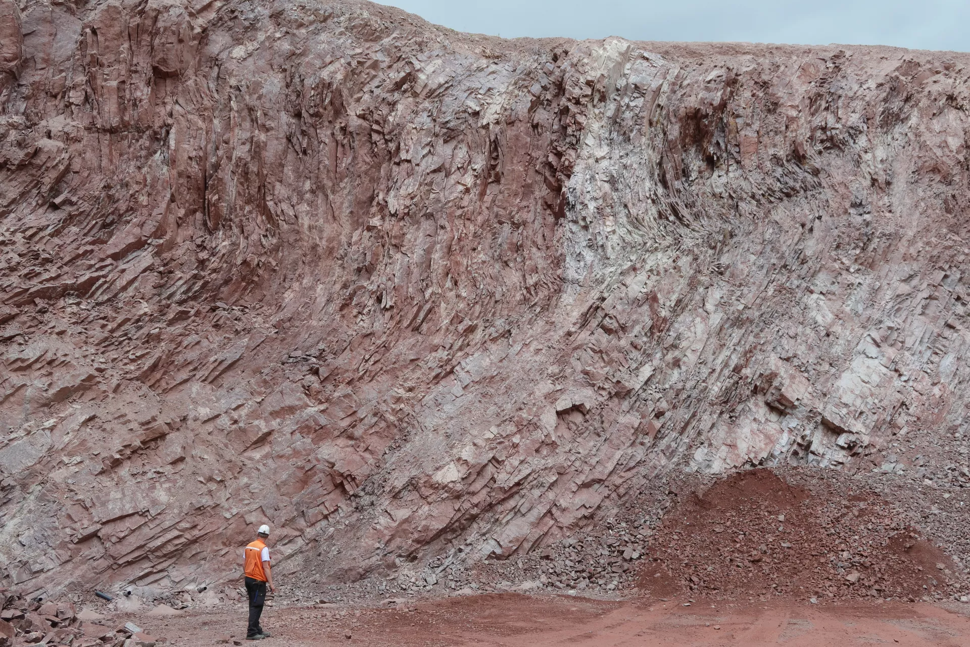 Eine Person steht links unterhalb der Bildmitte vor der etwa 15 Meter hohen Abbauwand des roten Granits.