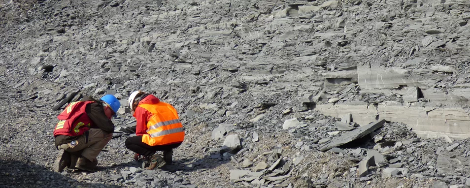Zwei Personen knien vor den grauen Schiefern in einem Steinbruch.