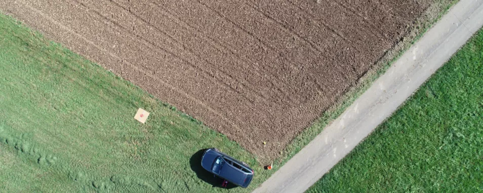 Luftbildaufnahme von Acker- und Grünlandflächen. Auf einer Wiese steht ein Auto. Davor liegt eine große quadratische Platte.